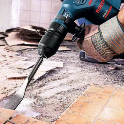 Pessoa a usar furadeira Bosch para raspar azulejos castanhos no chão e parede branca