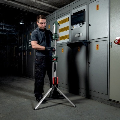 Homem ajustando tripé com ferramenta verde em ambiente industrial cinzento