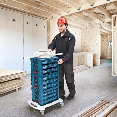 Carrinho branco com caixas azuis de plástico empilhadas em obra com operário de capacete vermelho