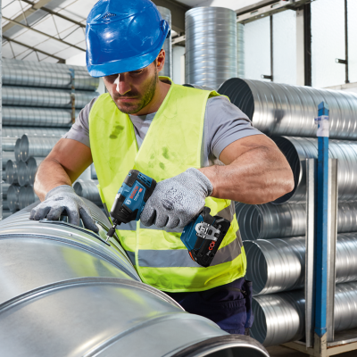 Homem a usar furadeira elétrica em tubos metálicos numa fábrica