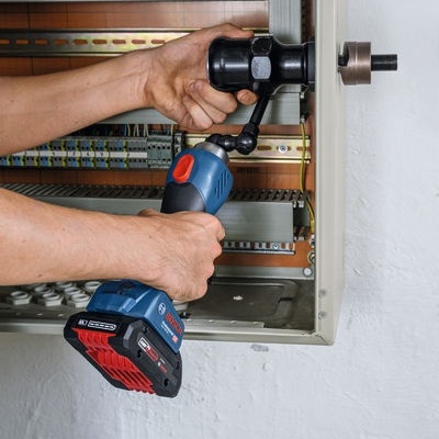 Mãos utilizando ferramenta elétrica Bosch num painel elétrico aberto.