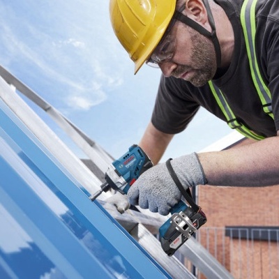 Homem a parafusar painéis metálicos azuis num telhado, usando equipamento de segurança