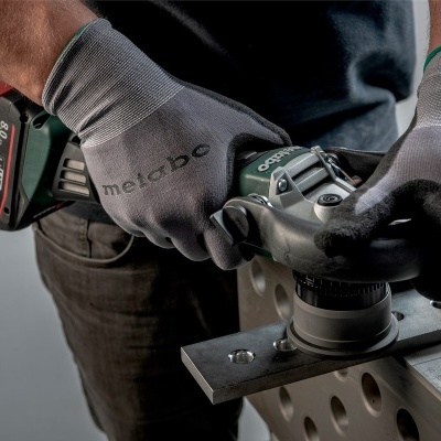 Aparelho esmerilhador Metabo preto e verde com luvas cinzentas a esmerilhar peça metálica preta com furos