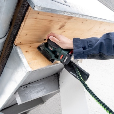 Pessoa a usar lixadeira elétrica preta e verde para lixar madeira num canteiro de obra exterior