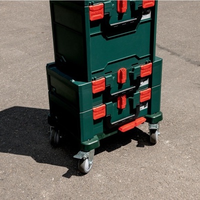 Caixa de ferramentas verde empilhada com fechos vermelhos e rodas sobre asfalto