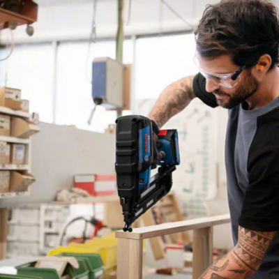 Homem a trabalhar com pistola pneumática azul e preta numa oficina.