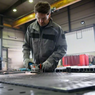 Homem com fato cinzento e preto a usar rebarbadora elétrica em placa metálica preta numa oficina