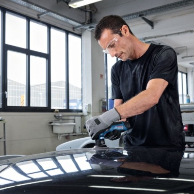 Homem a lixar capot de carro preto numa oficina com grandes janelas.