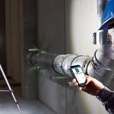 Homem com capacete azul a usar telemóvel perto de tubos e lanterna num tripé