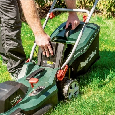 Aparelho corta-relvas elétrico Metabo em relvado verde com mão humana.