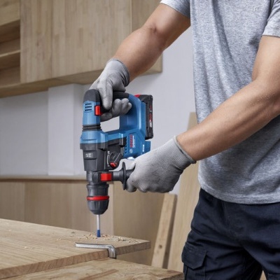 Pessoa a usar uma furadeira/parafusadeira azul em madeira clara