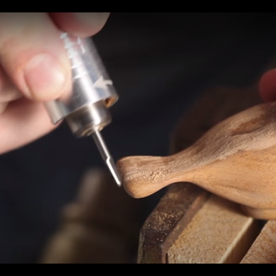 Pessoa a esculpir peça de madeira em forma de ave com ferramenta elétrica de precisão