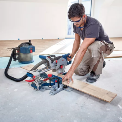 Homem a usar serra de esquadria elétrica com tábua de madeira num ambiente de construção interior