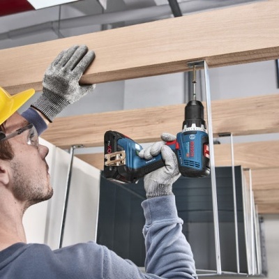 Homem com capacete amarelo usando parafusadora numa viga de madeira