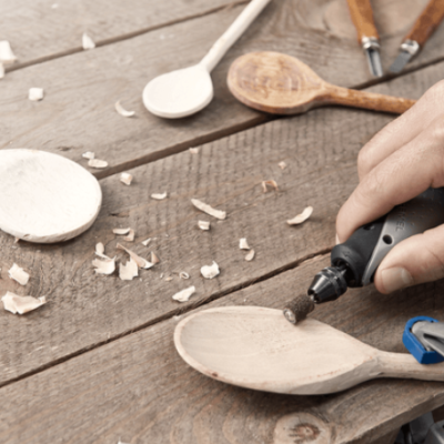 Mesa de madeira com colheres de madeira e ferramenta elétrica em uso para trabalhar uma colher