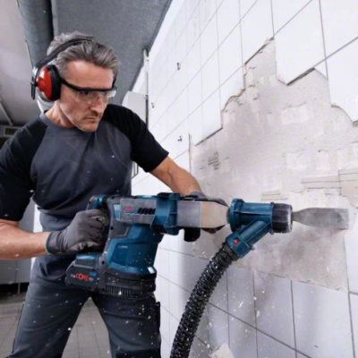 Homem a remover azulejos brancos com ferramenta elétrica azul, usando proteção de olhos e ouvidos