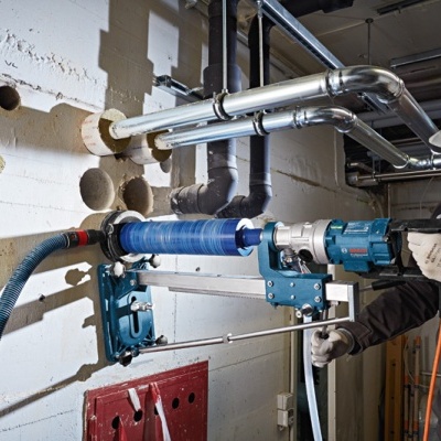 Homem a usar equipamento de perfuração industrial numa parede branca