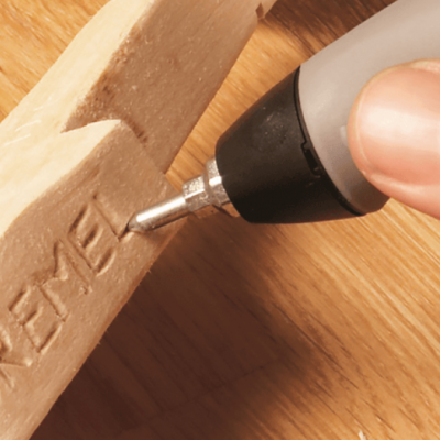 Ferramenta rotativa Dremel a gravar em madeira clara sobre superfície de madeira.