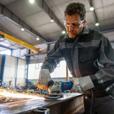 Homem a usar rebarbadora numa peça metálica numa oficina industrial