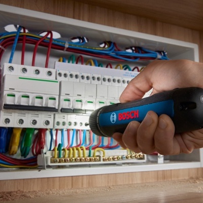 Painel elétrico com fios coloridos e detector de tensão BOSCH na mão