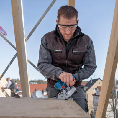 Homem a usar ferramenta elétrica para cortar madeira numa construção ao ar livre