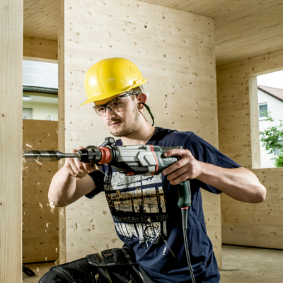 Homem com capacete amarelo a usar furadeira dentro de estrutura de madeira