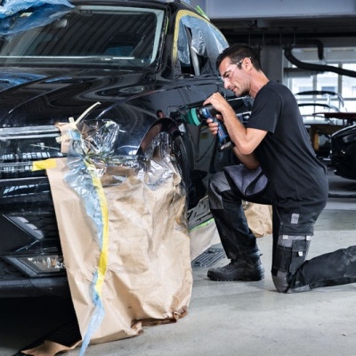 Homem a reparar carro preto numa oficina com proteção de papel e fita adesiva