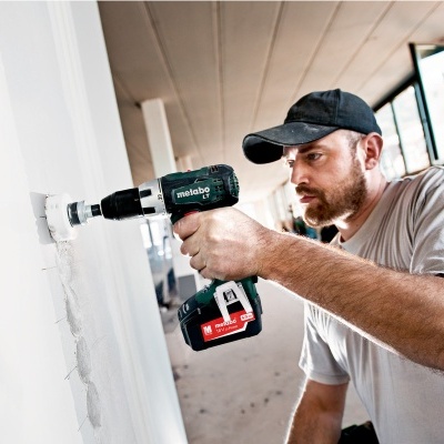 Homem a usar furadeira elétrica Metabo em parede branca dentro de edifício