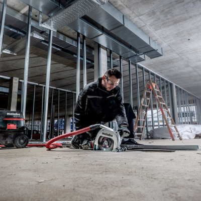 Operário a usar serra circular em obra com aspirador ao lado