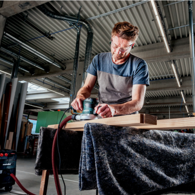 Homem a usar lixadeira elétrica em madeira numa oficina
