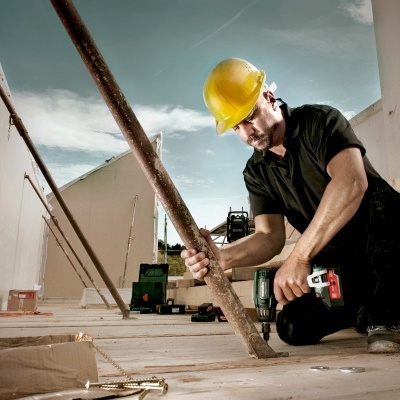 Trabalhador de construção com capacete amarelo a usar furadeira elétrica num canteiro de obras