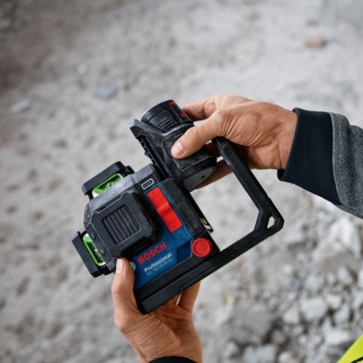 Pessoa segurando ferramenta Bosch azul, preta e vermelha com colete amarelo