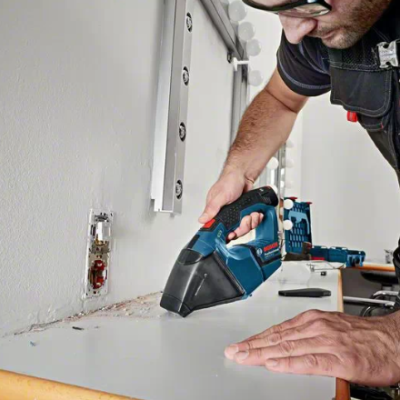 Pessoa usando ferramenta elétrica sem fios azul e preta para aparar tampo branco em ambiente interior