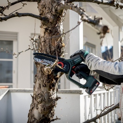 Pessoa a usar motosserra verde e preta para cortar árvore em frente a prédio branco