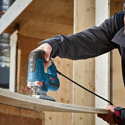 Homem a cortar prancha de madeira com serra tico-tico azul numa oficina