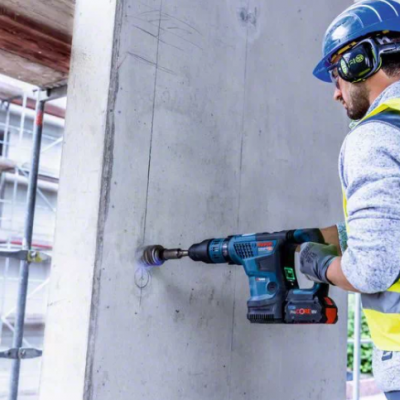 Trabalhador a usar furadeira elétrica numa parede de betão num local de construção