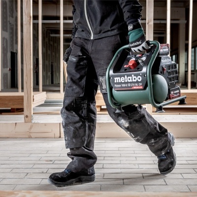 Pessoa com roupa de trabalho a carregar compressor METABO em obra interior