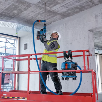 Trabalhador num andaime vermelho a usar ferramenta elétrica azul e preta no teto de betão.