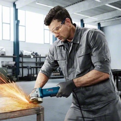 Homem a usar esmerilhadora elétrica azul em ambiente industrial