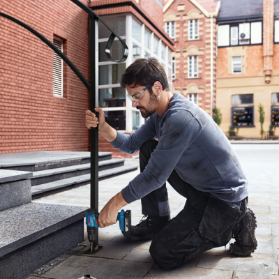 Homem a fixar corrimão metálico com furadeira em degraus exteriores urbanos