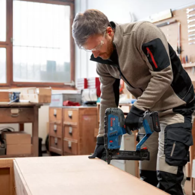 Homem a usar pistola de pregos azul e preta numa peça de madeira numa oficina