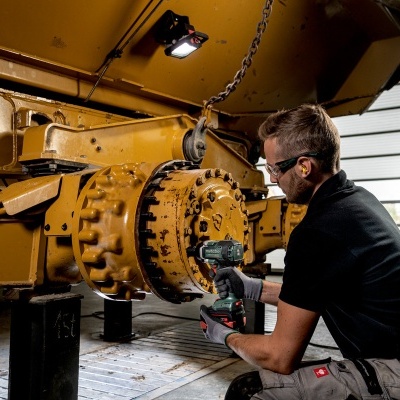 Homem a trabalhar numa peça metálica amarela com ferramenta elétrica numa oficina