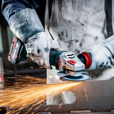 Pessoa a usar esmerilhadora elétrica com luvas e avental branco sujo, faíscas em superfície metálica