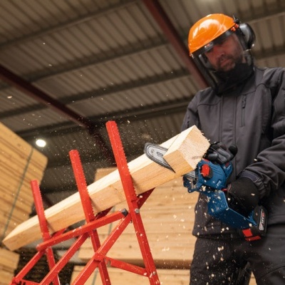 Homem com capacete e serra elétrica a cortar madeira numa estrutura vermelha