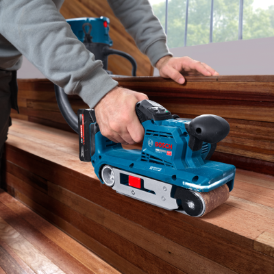 Lixadora de cinta Bosch azul a ser usada para alisar madeira.