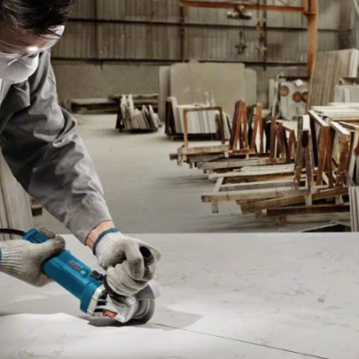 Pessoa a usar esmerilhadora num painel de mármore branco numa oficina