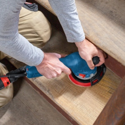 Pessoa a lixar degrau de madeira com lixadora elétrica azul