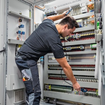 Homem a trabalhar em painel elétrico grande aberto com fios e disjuntores num ambiente industrial