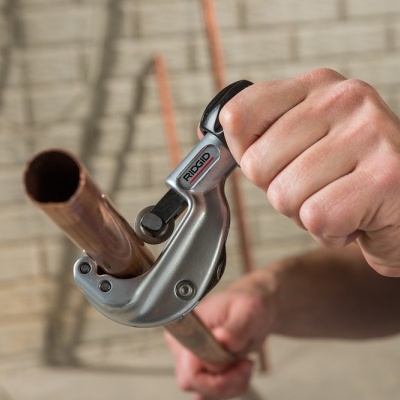 Ferramenta metálica cortando tubo de cobre em fundo de parede de tijolos