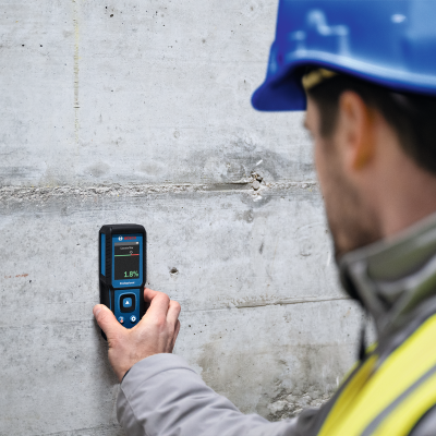 Homem a medir humidade numa parede de cimento com medidor BOSCH digital.